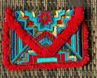 Clutch/Cross Body purse. The solid red back is accented with colorful shades of blue, red, and turquoise, complete with playful red tassel accents in the front. With the option to use the chain as a crossbody or keep it tucked in as a clutch, this bag is both fashionable and functional. Plus, there's a handy pocket inside!  SIZE: 12" X 9"