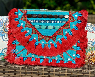 Make a statement with this larger Clutch/Cross Body Purse! This work of art features stunning bead work, a solid dark blue back, and pops of turquoise, shells, and accent beads. Use the chain to rock it as a crossbody or remove it for a chic clutch look. Bonus: red cotton tassels add an extra touch of fun!  SIZE: 13" X 10"