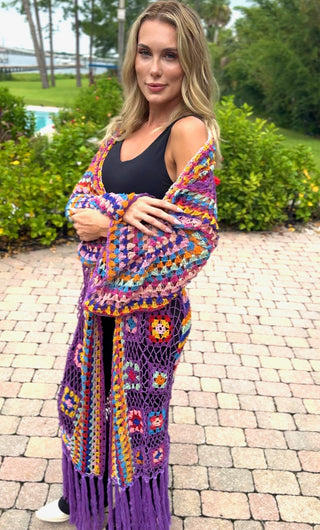 Tall woman wrapped in the rainbow crochet duster with purple fringe, worn over a black tank