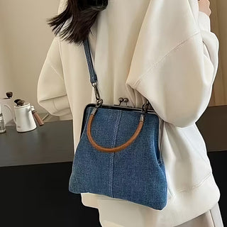 Person holding a blue denim handbag with a brown handle indoors.